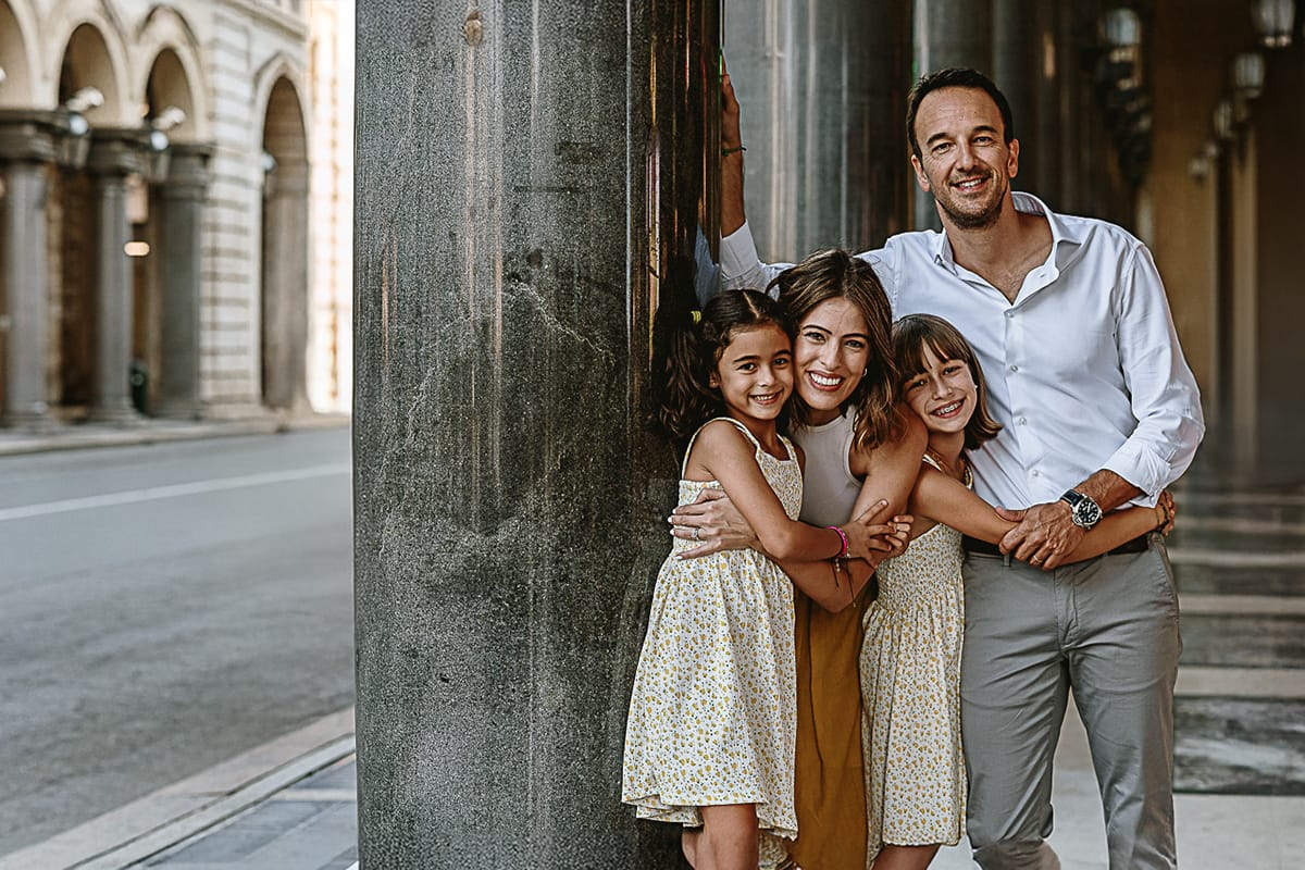 Fotografia di famiglia in vacanza a Torino: famiglia abbracciata sotto i portici di via Roma