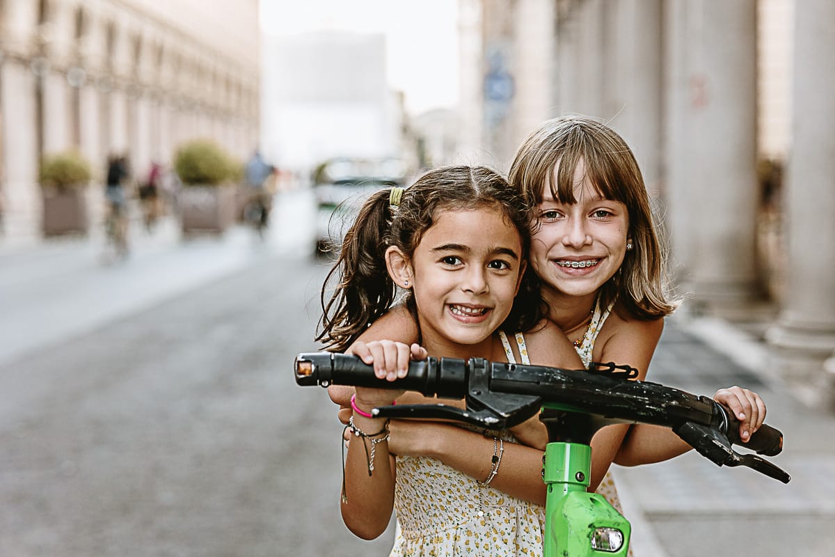 Fotografia di famiglia in vacanza a Torino: bambine su di un monopattino in via Roma