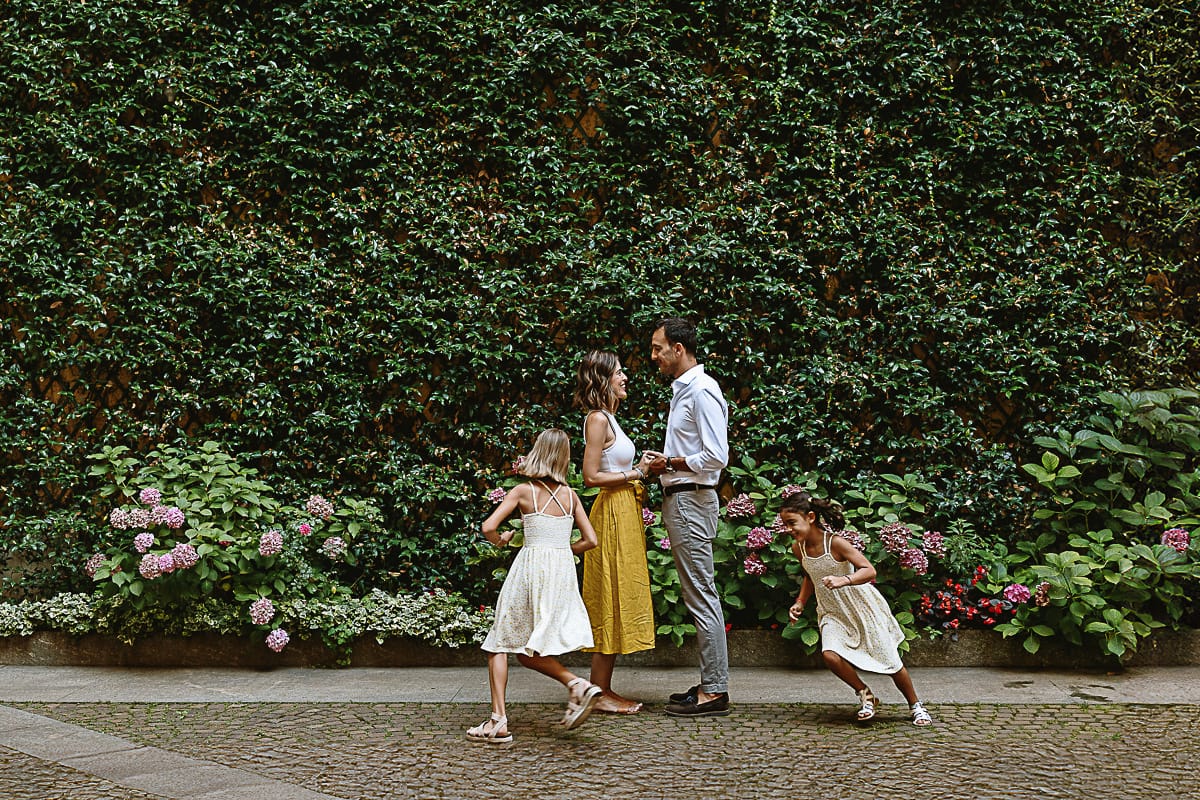 Fotografia di famiglia in vacanza a Torino: famiglia americane in un cortile di un palazzo del centro davanti ad una parete ricoperta di edera. I genitori si tengono per mano, le bambine corrono intorno a loro.