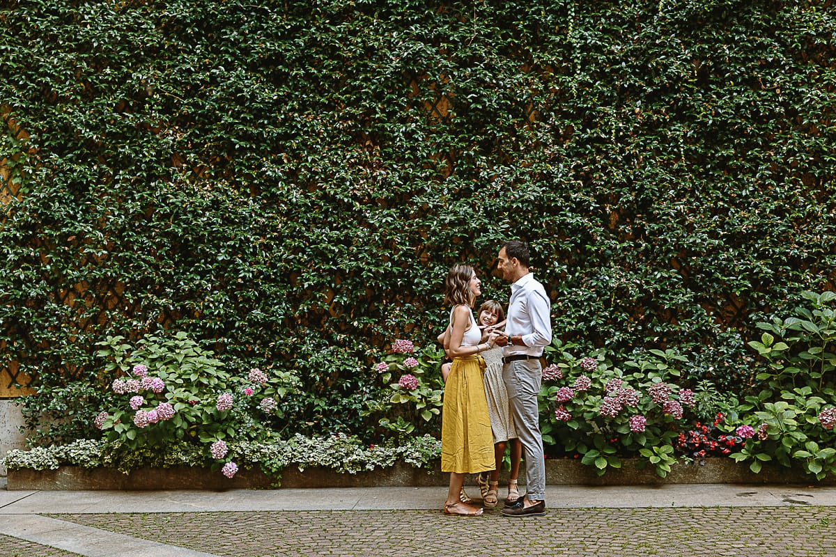 Fotografia di famiglia in vacanza a Torino: famiglia americane in un cortile di un palazzo del centro davanti ad una parete ricoperta di edera. I genitori si tengono per mano, la bambina dietro di loro li guarda divertita.