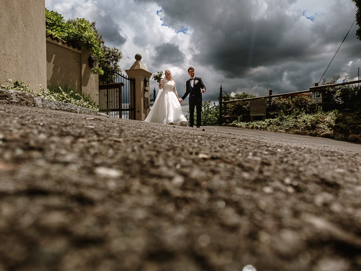 Fotografo matrimonio Torino. sposi camminano nel viale d'ingresso di Villa Ala. Sullo sfondo un bellissimo cielo drammatico pieno di nuvole anche se il tempo è soleggiato. Foto scattata dal drone posto per terra.