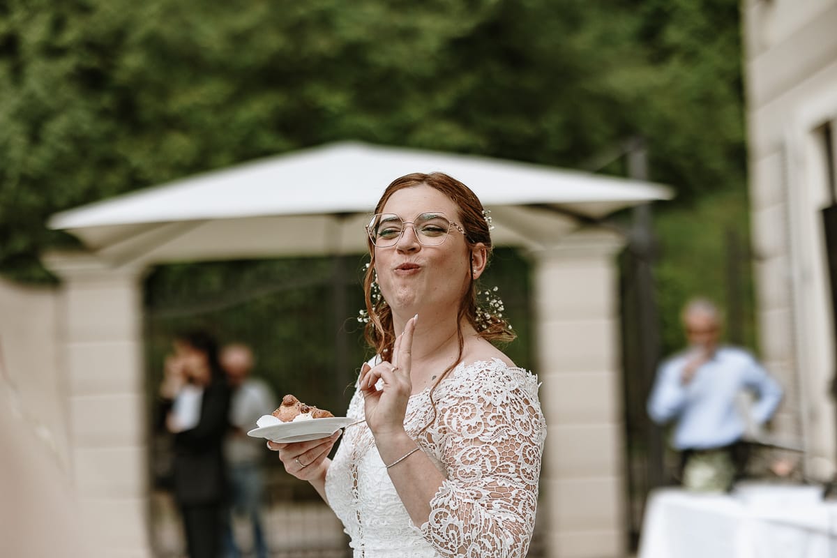 Fotografo matrimonio Torino. Momento aperitivo a Villa Ala. Sposa mangia con un piattino in mano ed un'espressione buffa.
