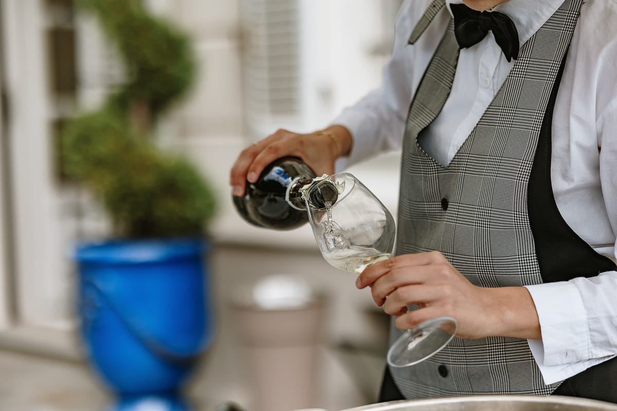 Fotografo matrimonio Torino. Momento aperitivo a Villa Ala. Un cameriere riempie un calice di vino bianco.