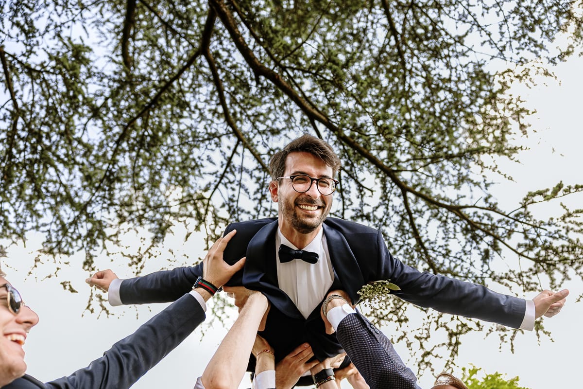 Fotografo matrimonio Torino. Momento aperitivo a Villa Ala. Amici sollevano lo sposo.