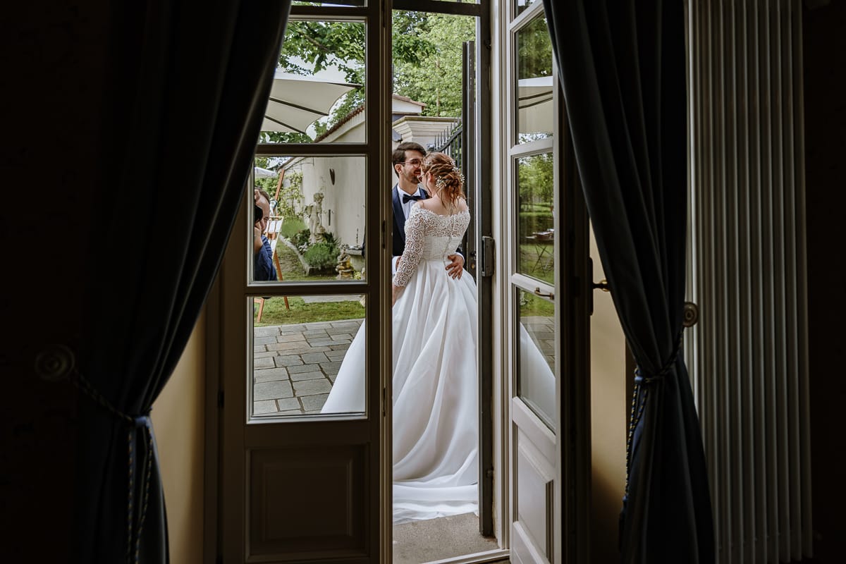 Fotografo matrimonio Torino. Momento aperitivo a Villa Ala. Sposi si guardano intensamente. Fotografati attraverso una porta finestra.