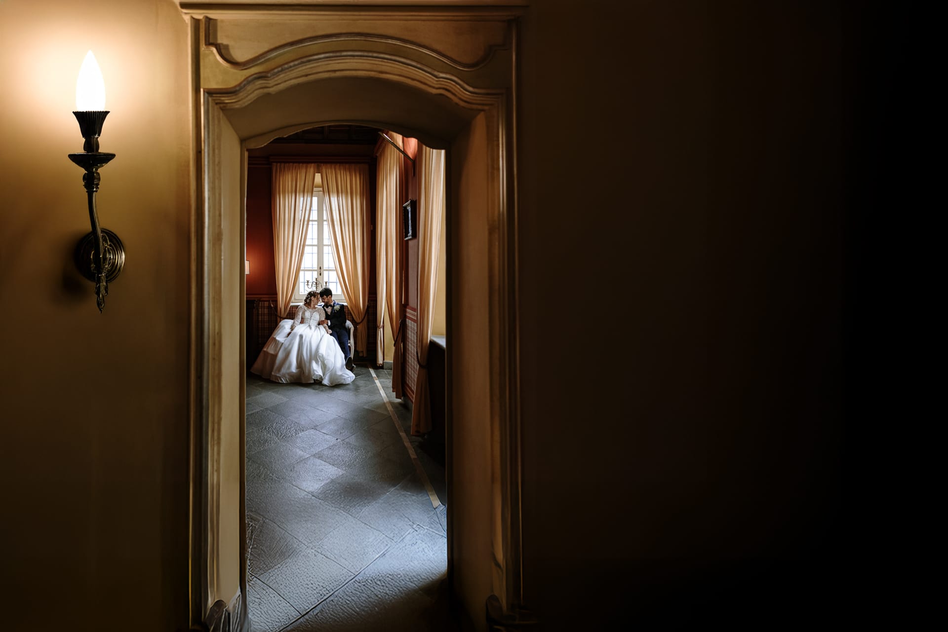 Fotografo Matrimonio Torino: Il Matrimonio di Giorgia e Marco a Villa Ala, Rivalba. Ritratto degli sposi seduti su di un divanetto in una bella sala di Villa Ala La foto è sta scattata da un'altra sala e quindi gli sposi sono incorniciati da una porta aperta.