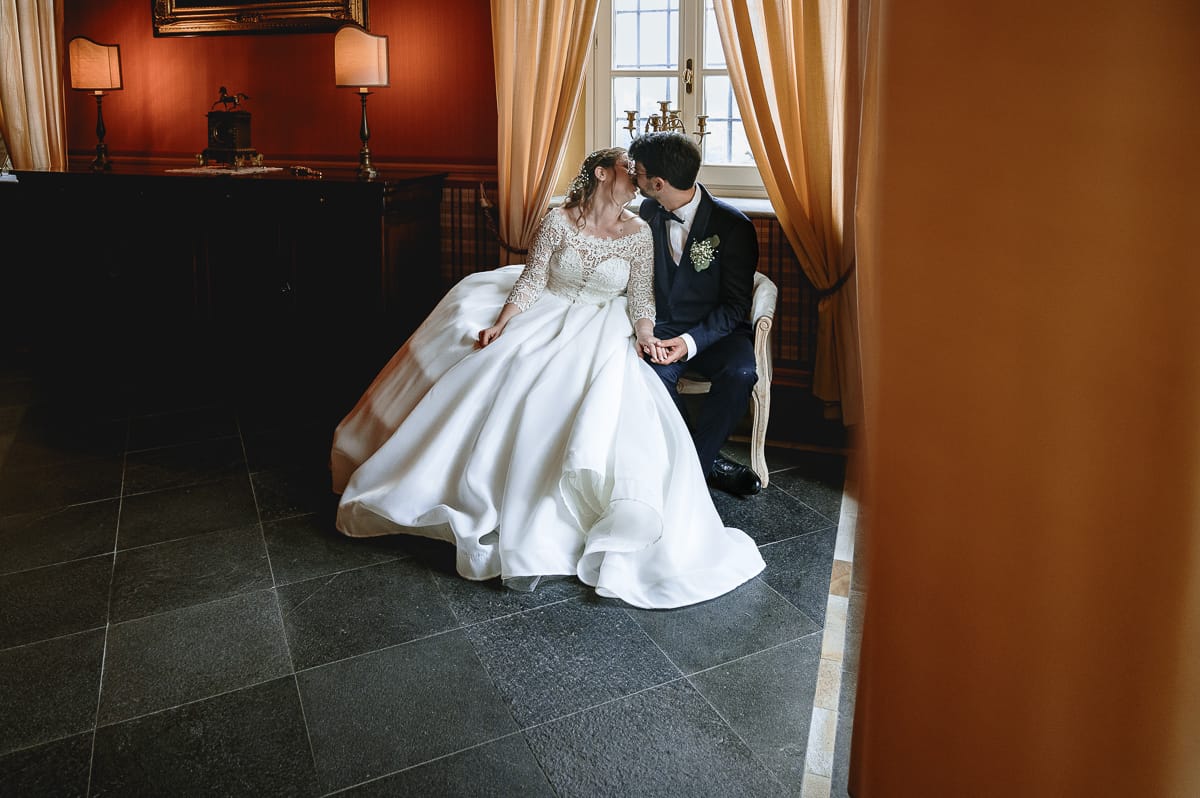 Fotografo matrimonio Torino. Ritratto degli sposi seduti su di un divano che si baciano in una bella sala di Villa Ala.