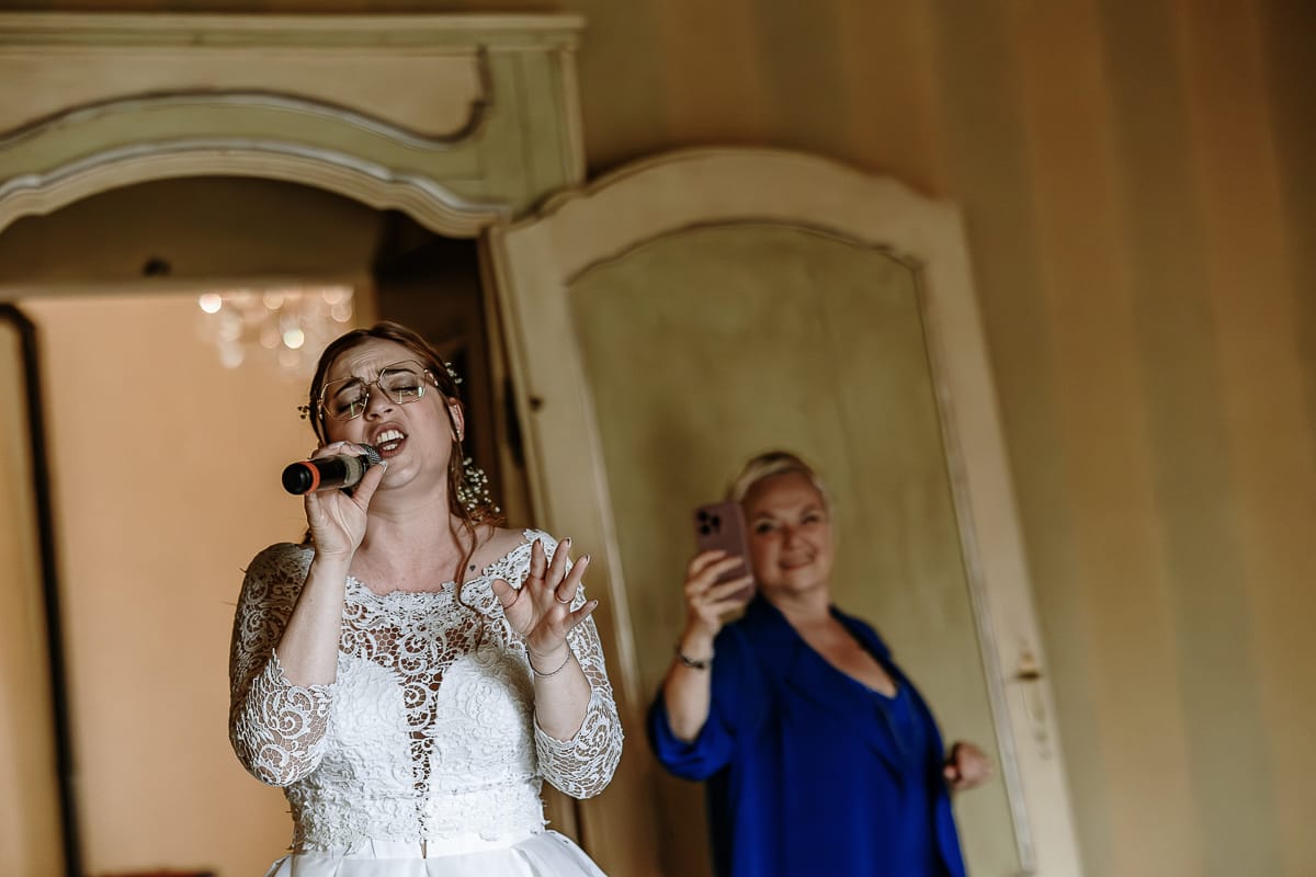 Fotografo matrimonio Torino. La sposa canta nel salone delle feste di Villa Ala. la mamma dietro di lei la filma con il cellulare.