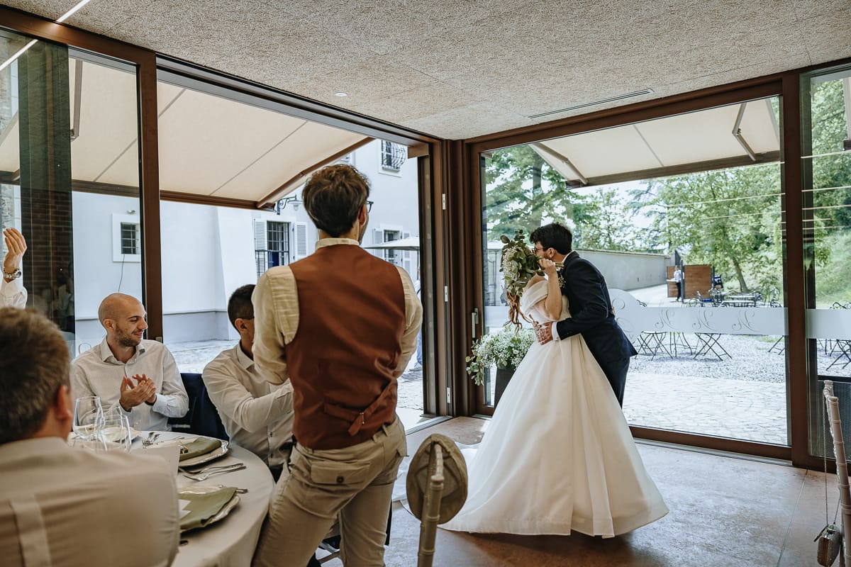 Fotografo matrimonio Torino. Gli sposi si baciano appassionatamente nella veranda di Villa Ala dove si svolge il pranzo nuziale. Gli invitati applaudono