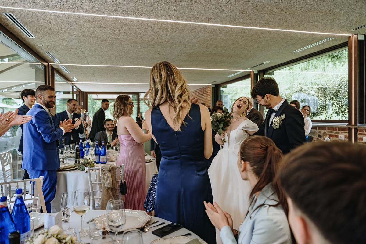 Fotografo matrimonio Torino. Ingresso degli sposi nella zona pranzo di Villa Ala. La sposa ride, gli invitati applaudono.