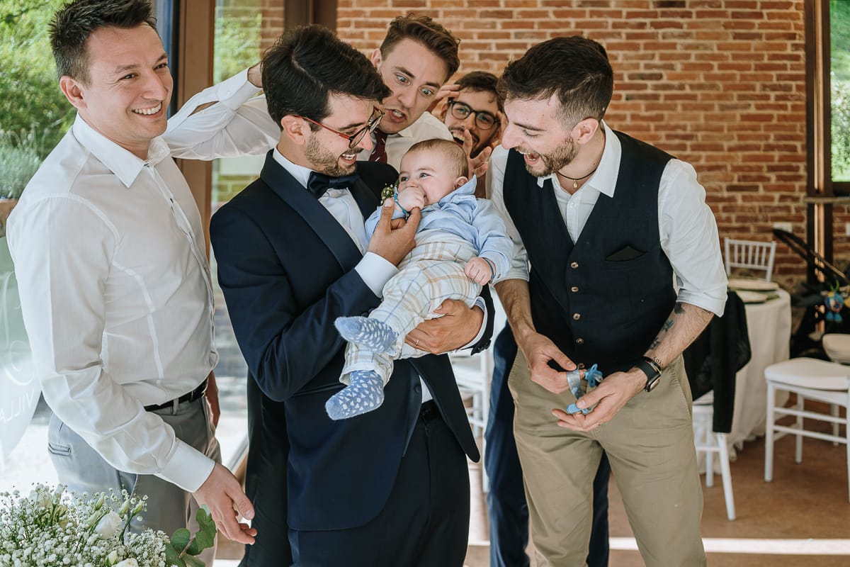 Fotografo matrimonio Torino. Pranzo nuziale a Villa Ala. Sposo con gli amici e un neonato in braccio.