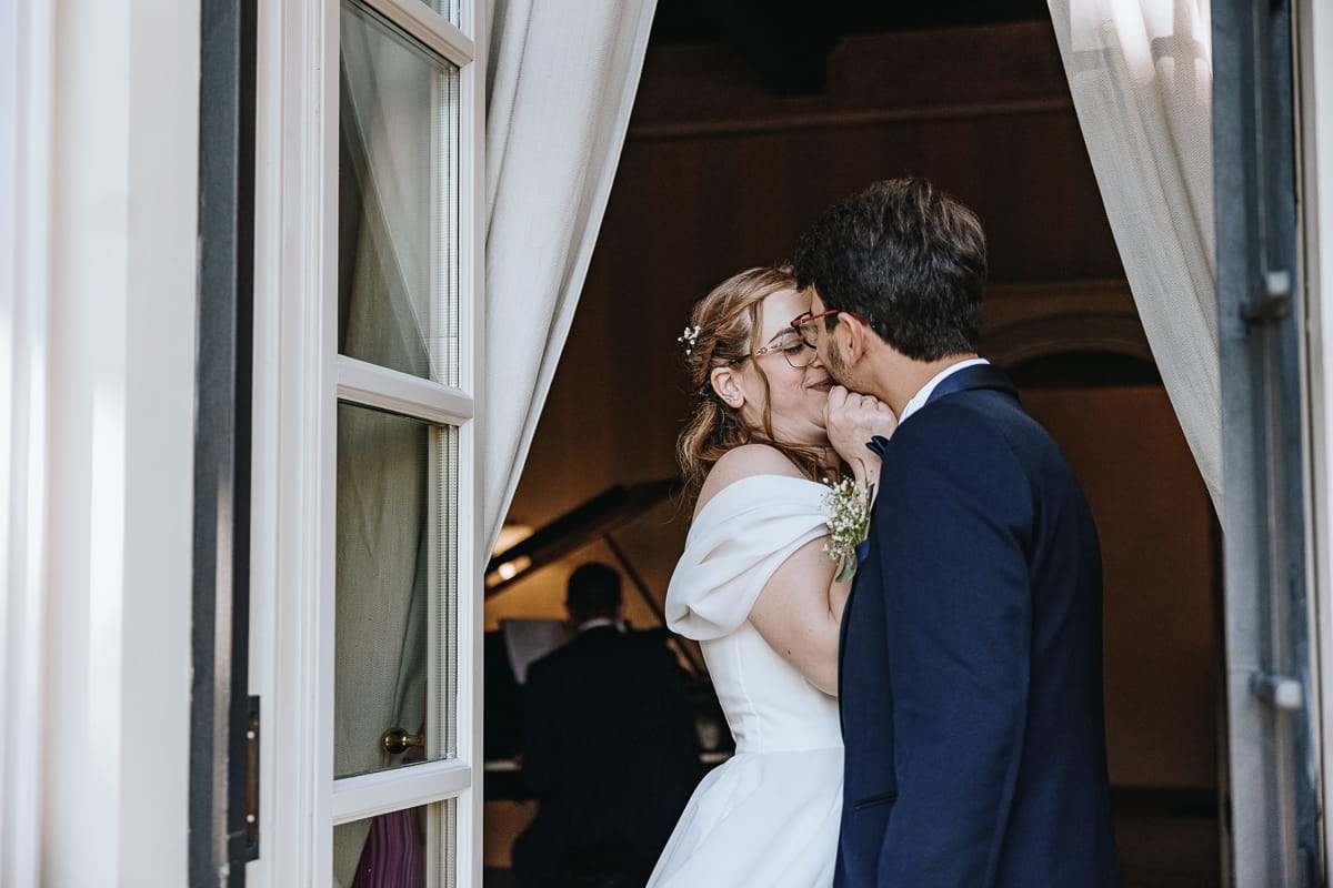 Fotografo matrimonio Torino. Ritratto tenero degli sposi in una sal di Villa Ala, mentre un musicista suona il pianoforte.