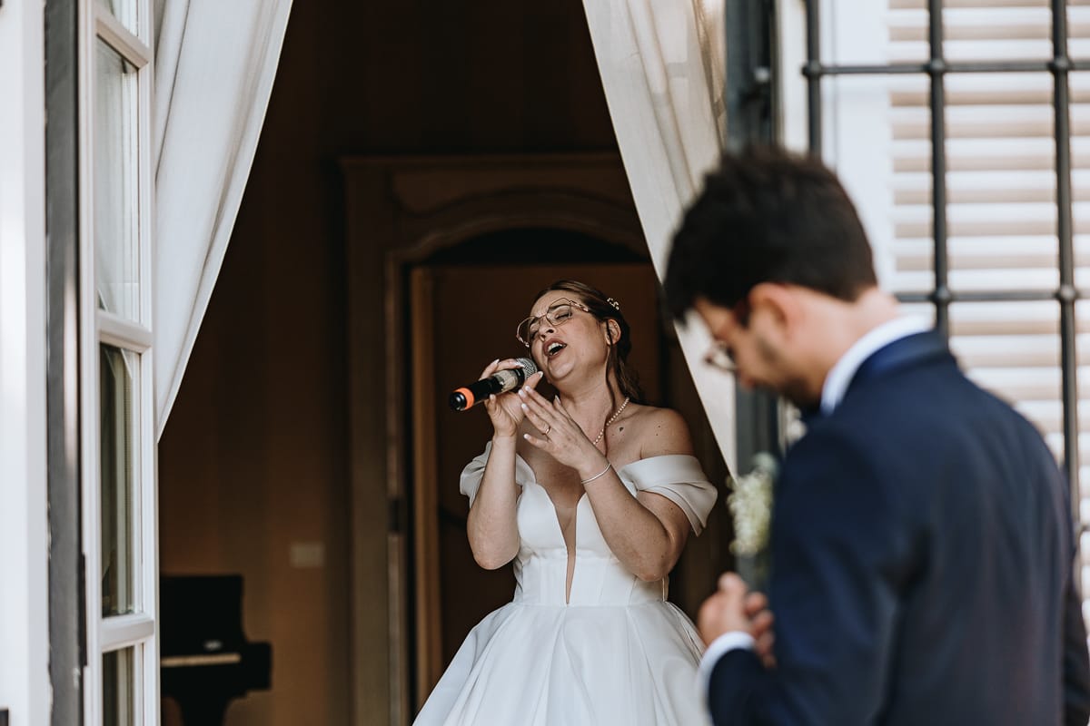 Fotografo matrimonio Torino. La sposa canta con passione in una sala di Villa Ala mentre lo sposo la guarda.
