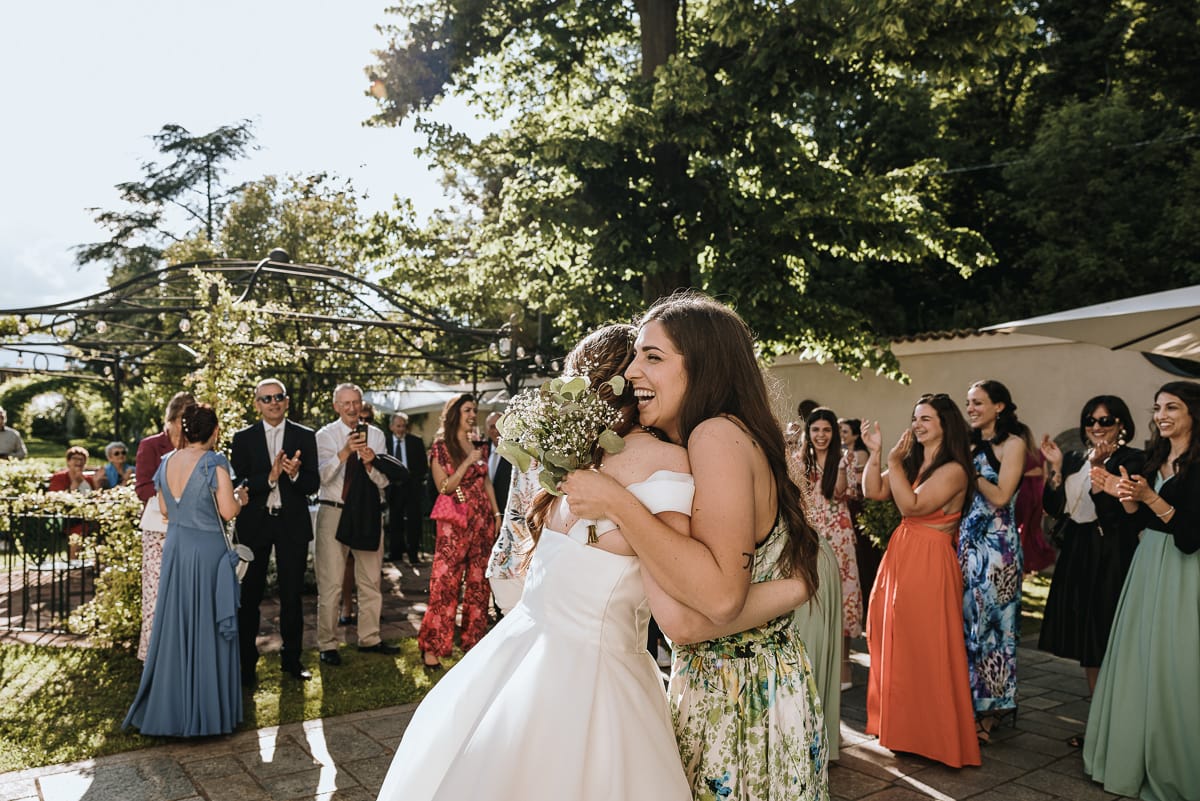 Fotografo matrimonio Torino. La sposa abbraccia la ragazza che ha preso il bouquet nel giardino di Villa Ala.