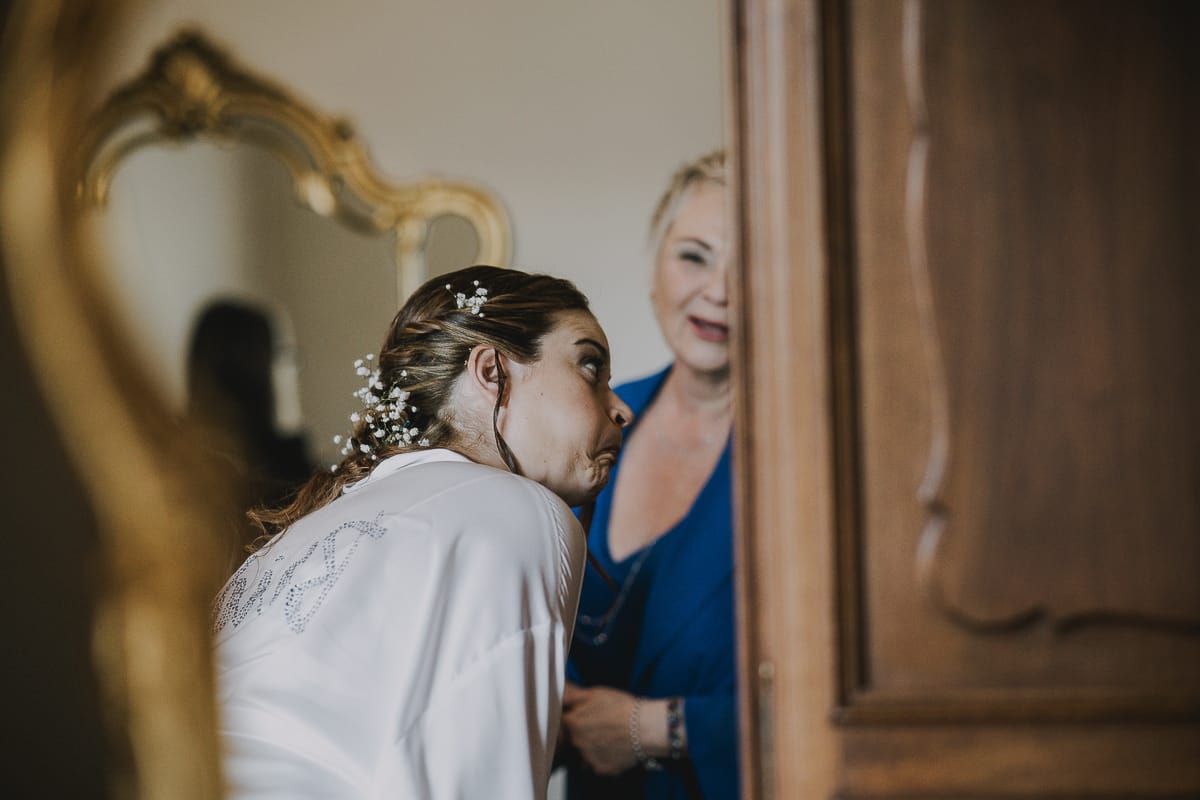 Preparazione della sposa a Madonna della Scala. Sposa con un'espressione buffa riflessa in uno specchio con la mamma.
