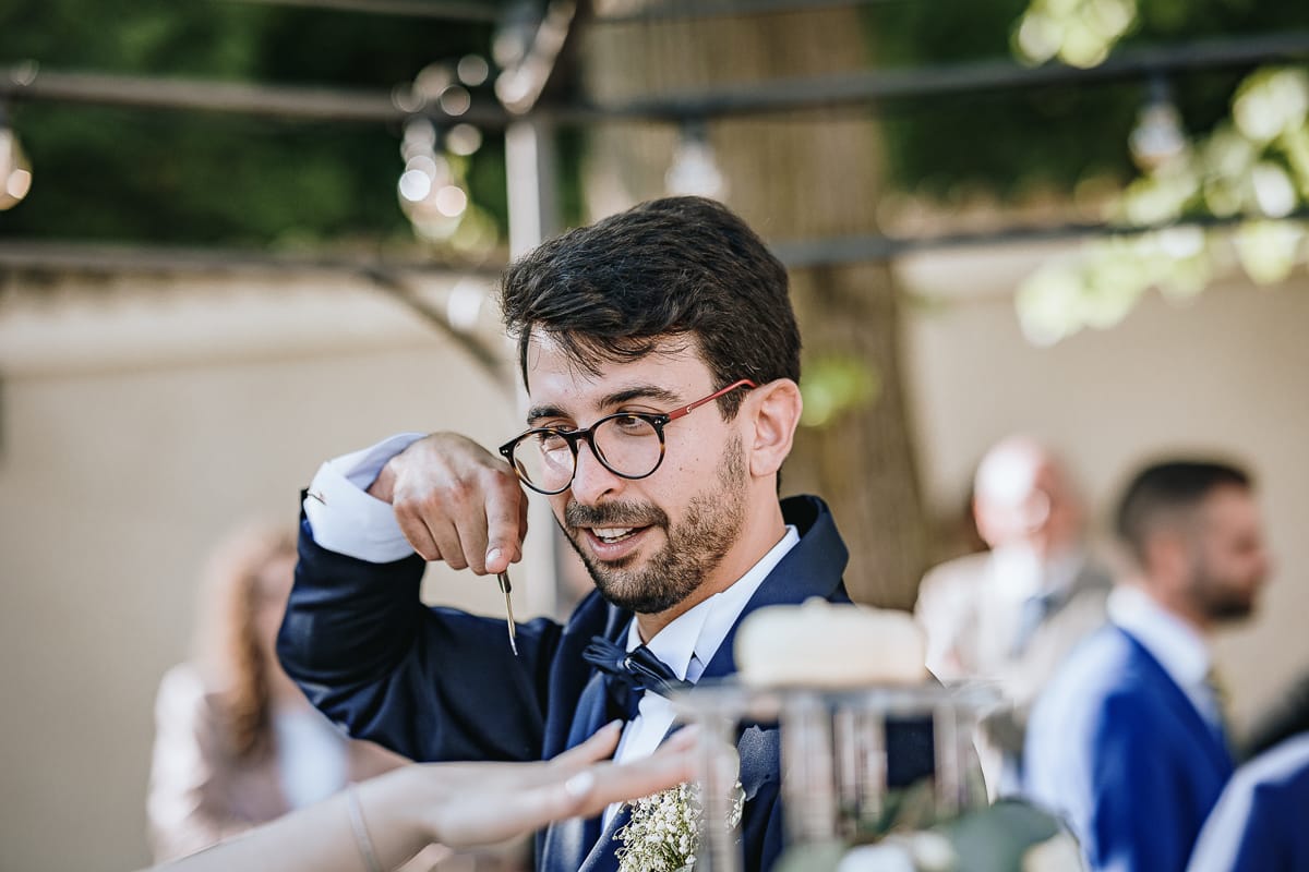 Fotografo matrimonio Torino. Taglio della torta sotto un gazebo nel giardino di Villa Ala. Sposo impugna il coltello con un'espressione buffa.