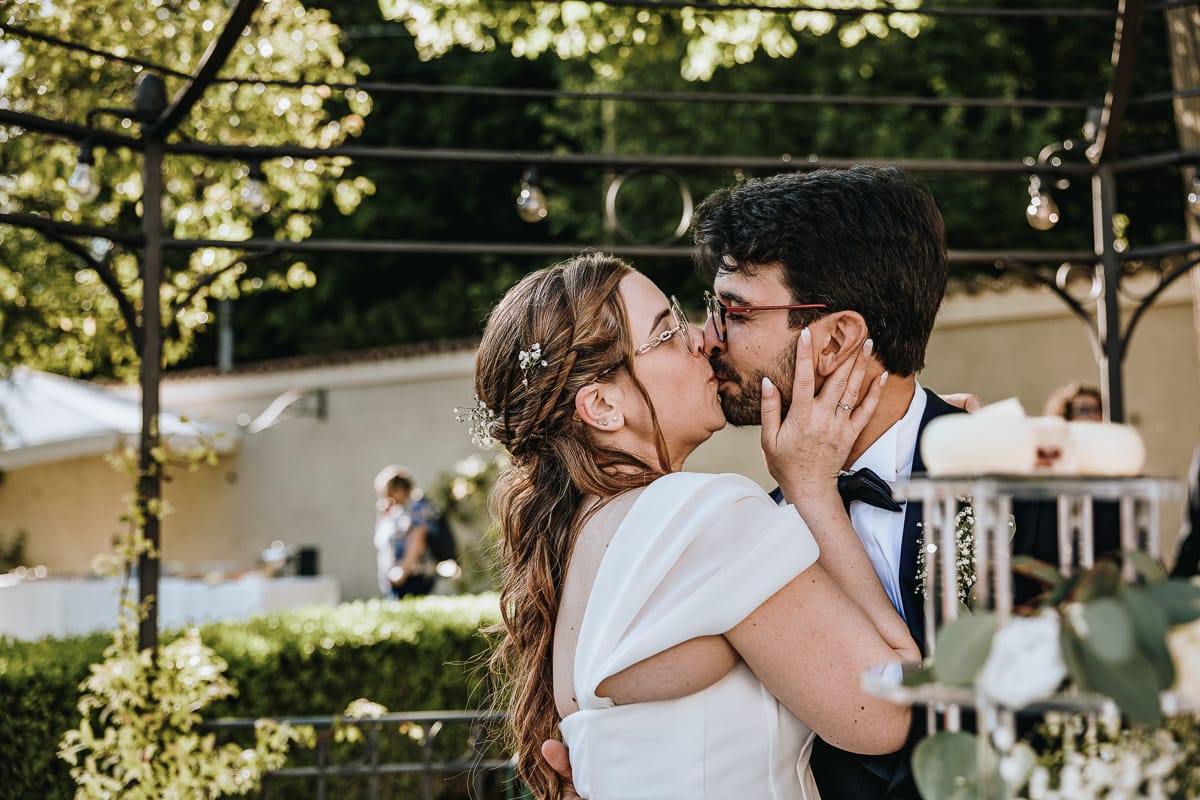 Fotografo matrimonio Torino. Taglio della torta sotto un gazebo nel giardino di Villa Ala. Gli sposi si baciano.