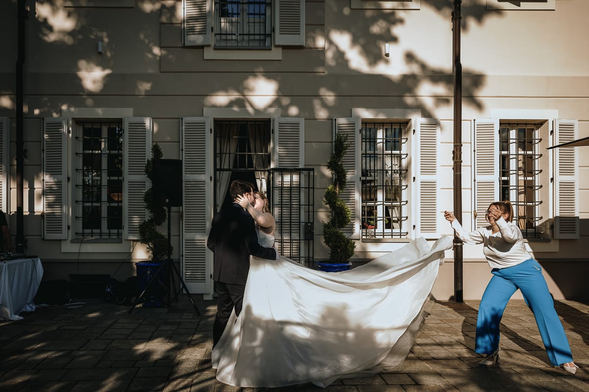 Fotografo matrimonio Torino. Gli sposi si baciano sul patio di Villa ala, mentre la sorella dello sposo fa volare la gonna della sposa.