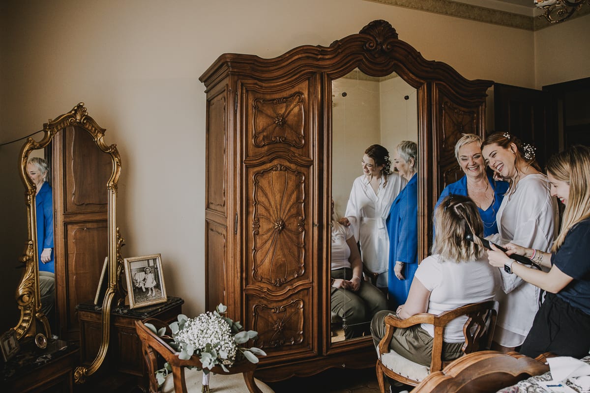 Preparazione della sposa a Madonna della Scala. Sposa e mamma riflesse in uno specchio guardano la sorella che viene pettinata.