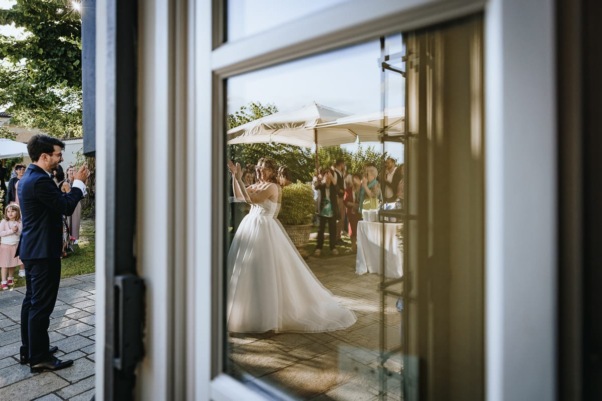 Fotografo matrimonio Torino. Ballo degli sposi con i genitori nel patio di Villa Ala. sposo applaude. anche la sposa applaude mentre è riflessa in una porta finestra.