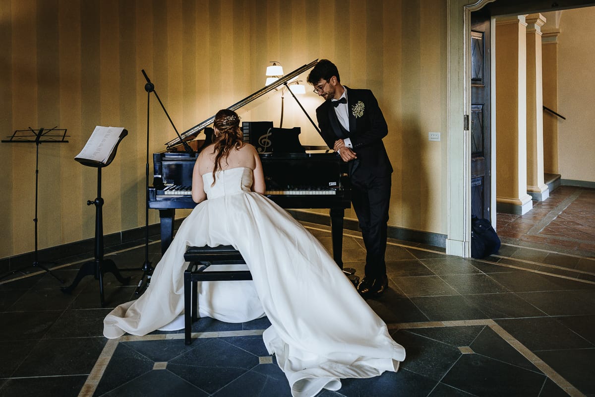 Fotografo matrimonio Torino. La sposa suona il pianoforte a coda in una sala di Villa Ala. Lo sposo la ascolta con amore.