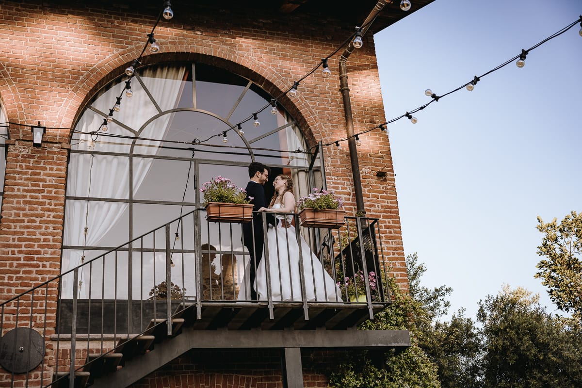 Fotografo matrimonio Torino. Gli sposi si baciano nell'ex fienile di Villa ala. mentre la loro silhouette si riflette nella vetrata al tramonto.