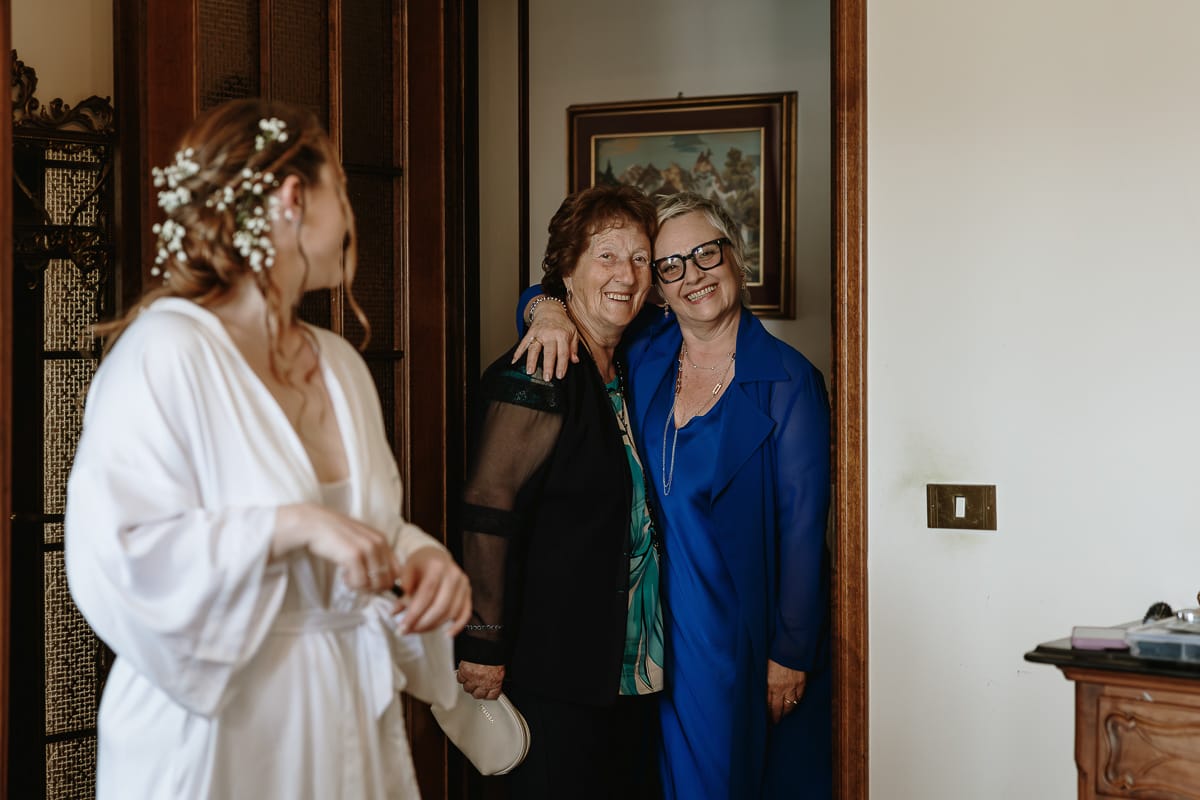 Preparazione della sposa a Madonna della Scala. Sposa guarda la nonna e la mamma abbracciate.