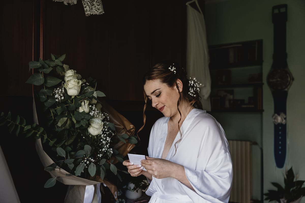 Preparazione della sposa a Madonna della Scala. Sposa legge il biglietto che accompagna le rose dello sposo