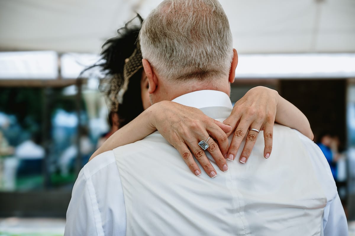 Fotografo matrimonio in Monferrato. Matrimonio di Serena e Fabrizio al Vecchio Castagno di Cocconato d'Asti. Pranzo nuziale. Ballo degli sposi.Dettagli sulle mani della sposa al collo dello sposo.