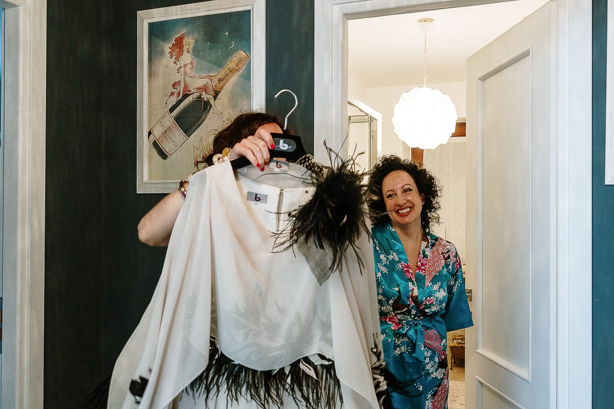 Fotografo matrimonio in Monferrato. Matrimonio di Serena e Fabrizio. Preparazione a Baldissero Torinese. Sorella della sposa tiene in mano il vestito della sposa mentre la sposa la guarda.