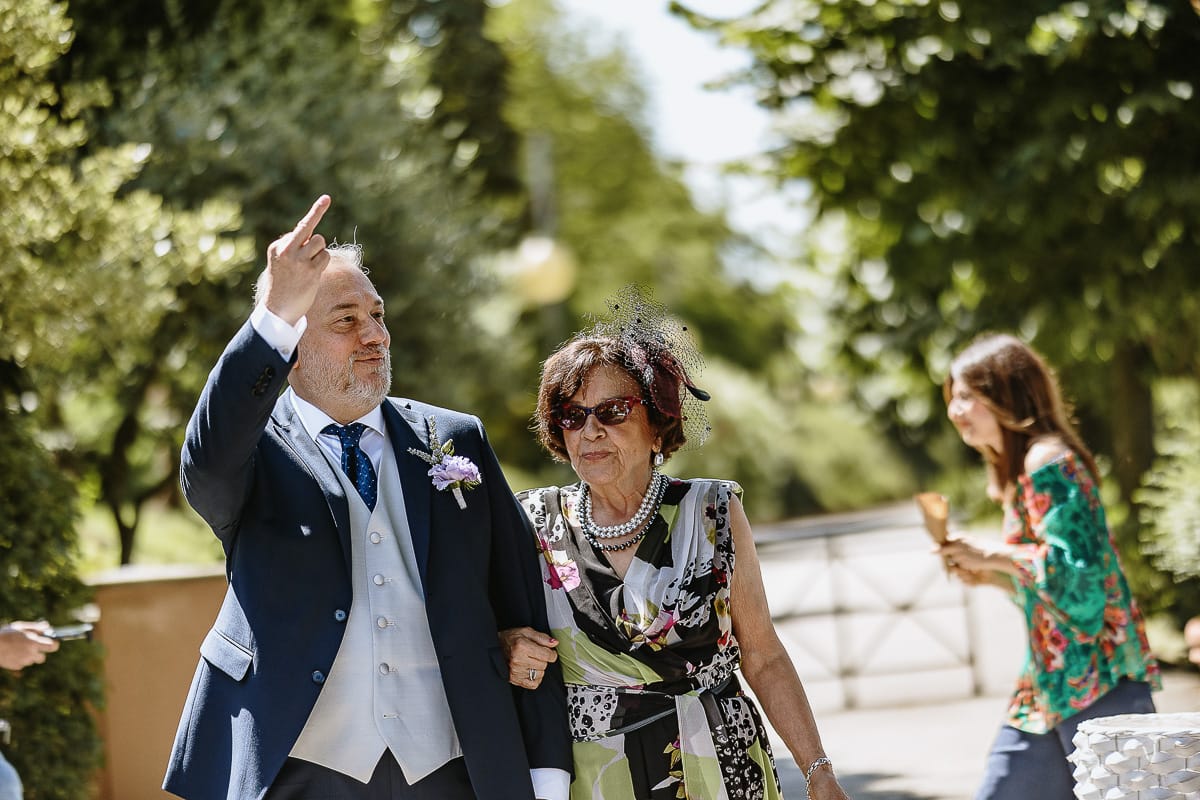 Fotografo matrimonio in Monferrato. Matrimonio di Serena e Fabrizio al Vecchio Castagno di Cocconato d'Asti.Sposo si dirige verso la zona della cerimonia al braccio della suocera mostrando il dito medio.