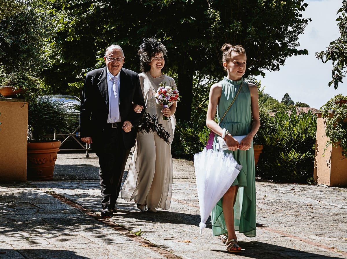 Fotografo matrimonio in Monferrato. Matrimonio di Serena e Fabrizio al Vecchio Castagno di Cocconato d'Asti. Sposa si dirige verso il luogo della cerimoni al braccio del padre. davanti c'è la nipotina.