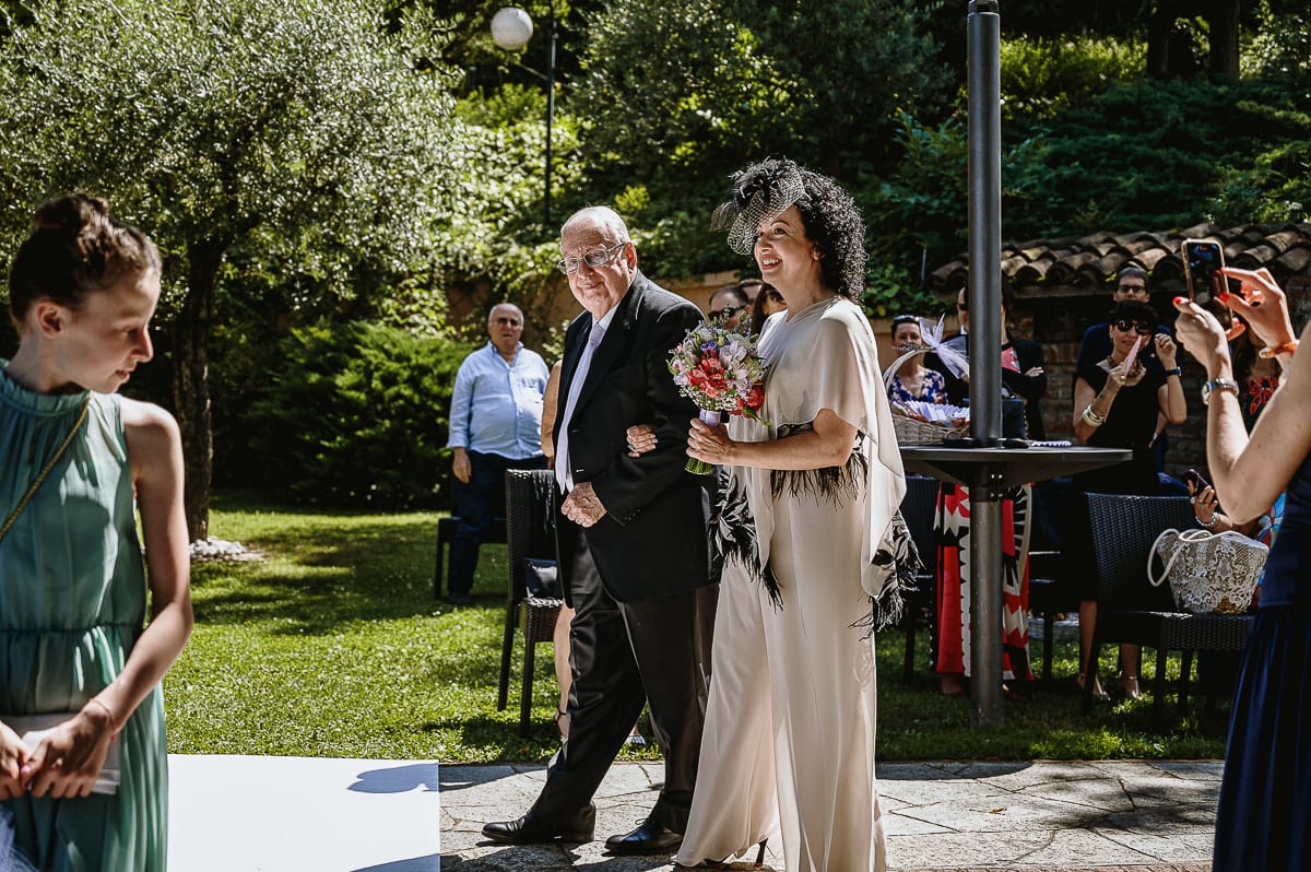 Fotografo matrimonio in Monferrato. Matrimonio di Serena e Fabrizio al Vecchio Castagno di Cocconato d'Asti. Sposa si dirige verso il luogo della cerimonia al braccio del padre.
