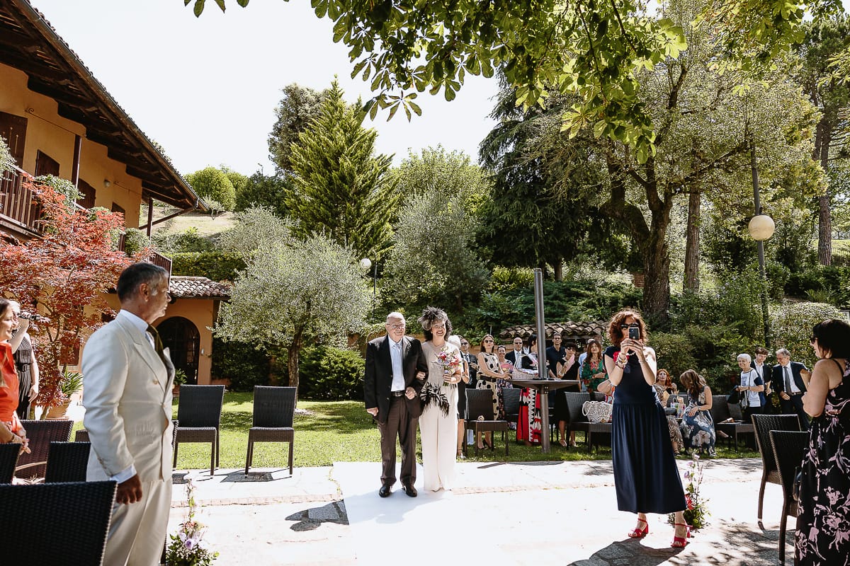 Fotografo matrimonio in Monferrato. Matrimonio di Serena e Fabrizio al Vecchio Castagno di Cocconato d'Asti. Sposa si dirige verso il luogo della cerimonia al braccio del padre.