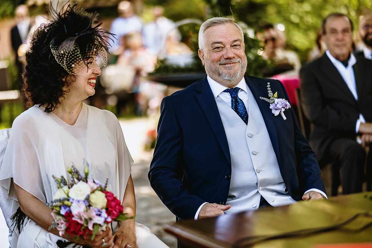 Fotografo matrimonio in Monferrato. Matrimonio di Serena e Fabrizio al Vecchio Castagno di Cocconato d'Asti. Cerimonia. Sposa sorridente guarda lo sposo che ride con una buffa espressione.
