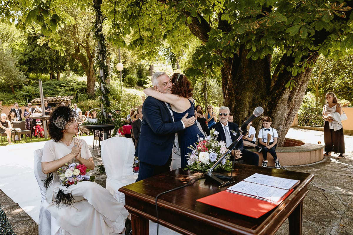 Fotografo matrimonio in Monferrato. Matrimonio di Serena e Fabrizio al Vecchio Castagno di Cocconato d'Asti. Cerimonia. Sorella della sposa abbraccia lo sposo.