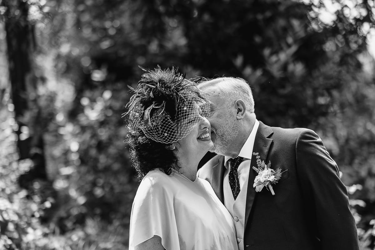 Fotografo matrimonio in Monferrato. Matrimonio di Serena e Fabrizio al Vecchio Castagno di Cocconato d'Asti. Ritratti di coppia degli sposi. Sposo bacia la sposa sulla guancia. Bianco enero.