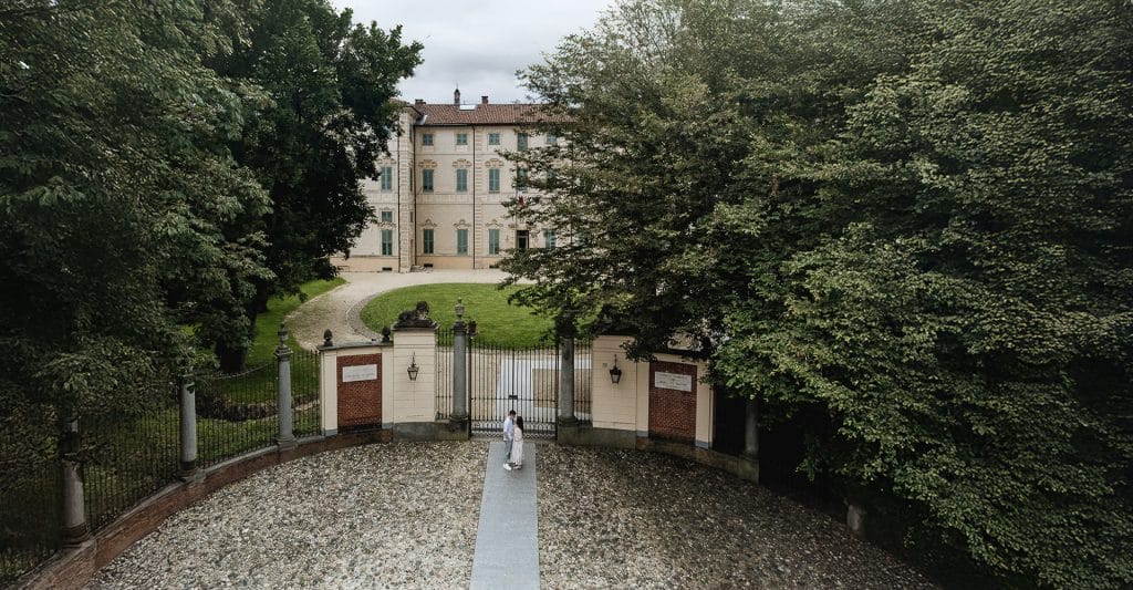 A magical pre-wedding moment at Cavour Castle in Santena. Fabiola and Cristian stand before the castle gate, with the castle and park as their stunning backdrop. Captured from above by a drone  