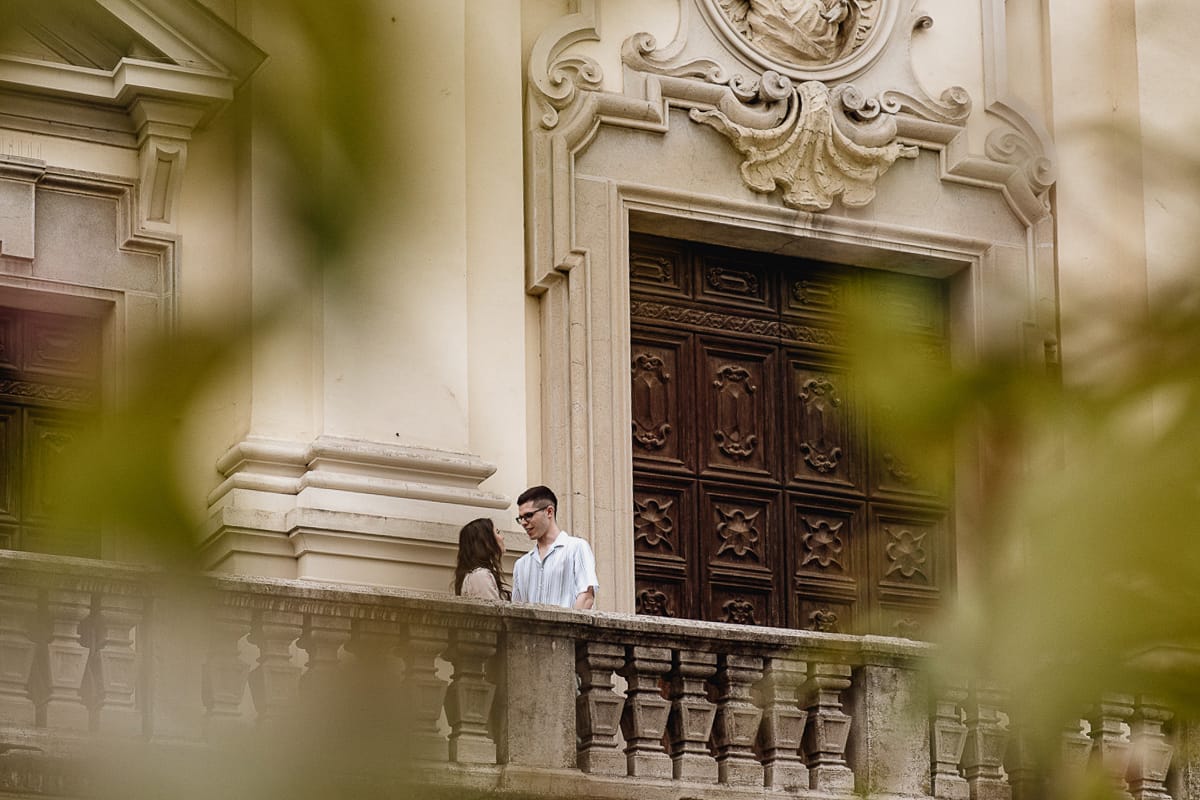 Pre-wedding al Castello di Santena. Fabiola e Cristian sulla scalinata della chiesa si guardano. Foto scattata attraverso delle piante.