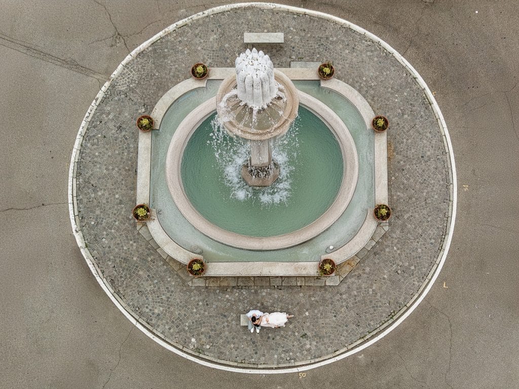 Fabiola and Cristian pose on a stone bench in front of the fountain during their pre-wedding at Castello di Santena. 