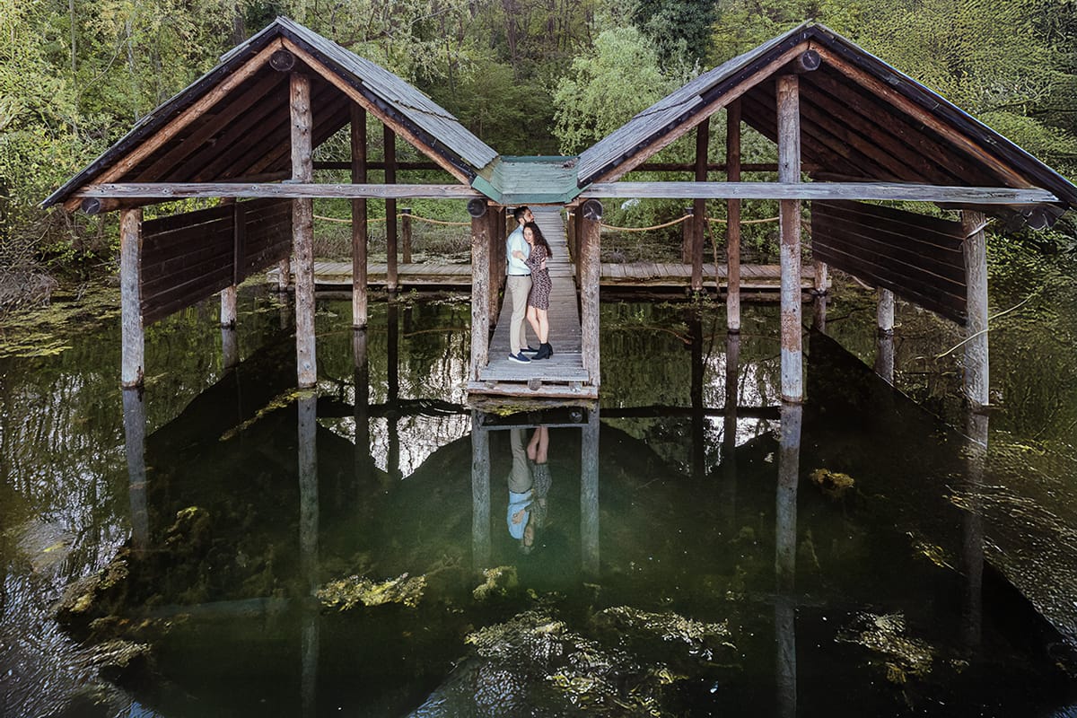 Pre-wedding al Lago di Viverone di Ilaria e Luca. Foto aerea dal drone della coppia tra le palafitte. La coppia è riflessa nel lago.