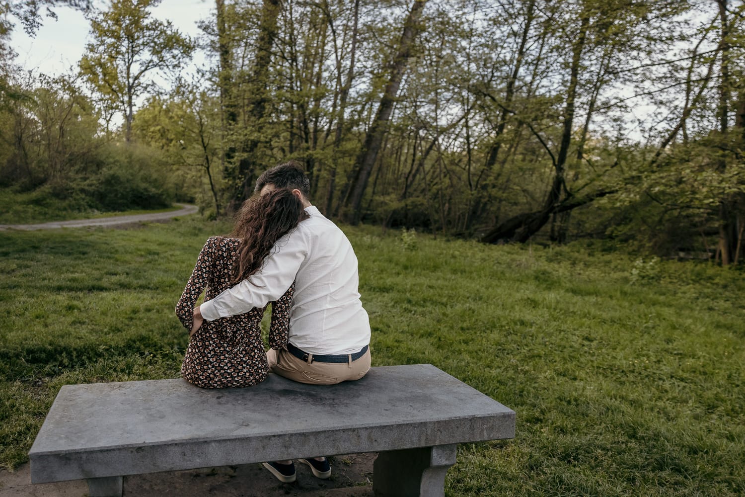 Pre-wedding al Lago di Viverone di Ilaria e Luca. Foto della coppia seduta su di una panchina in pietra davanti alla zona delle palafitte. Fotografati di schiena.