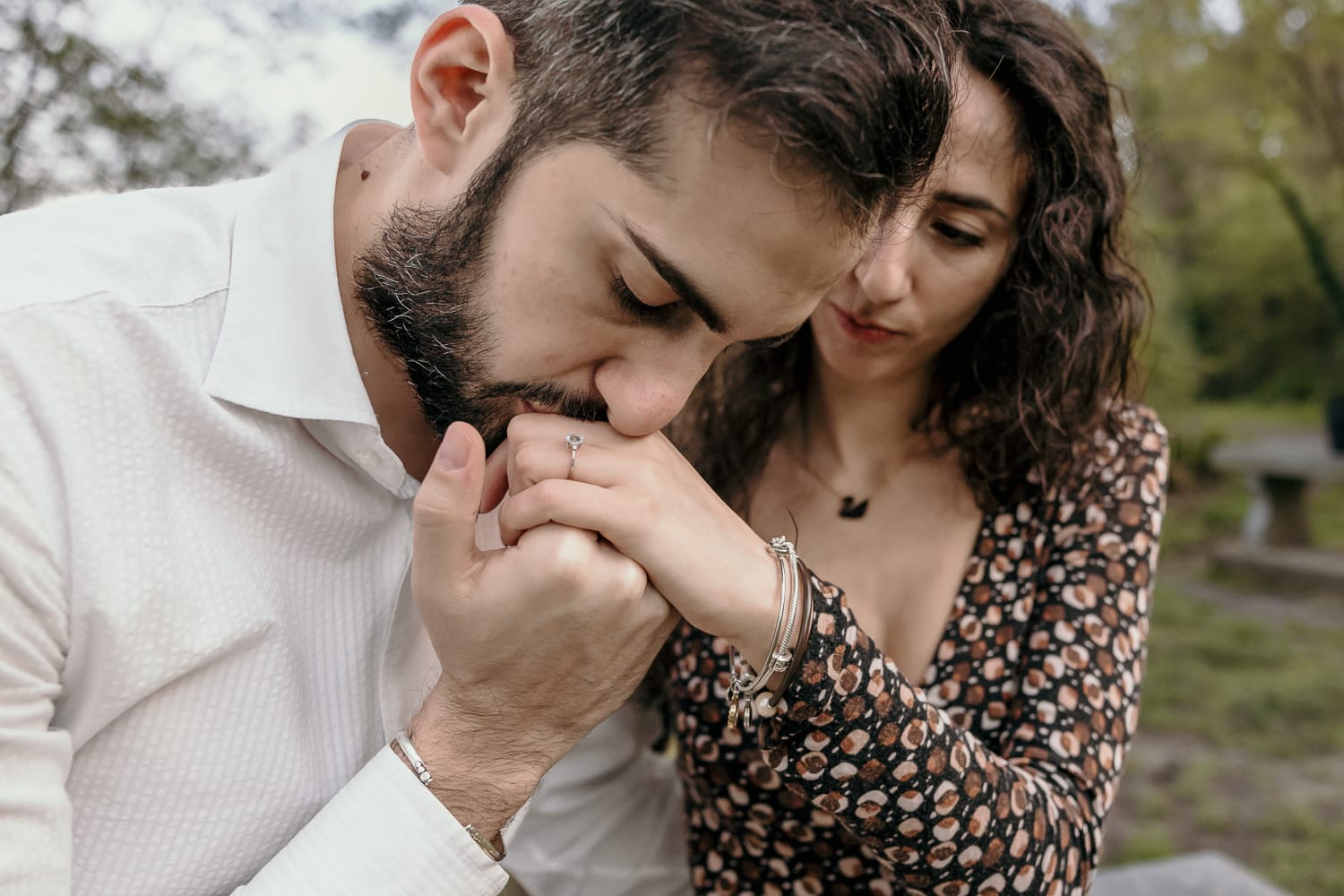 Pre-wedding al Lago di Viverone di Ilaria e Luca. Foto della coppia seduta su di una panchina in pietra davanti alla zona delle palafitte. Luca bacia la mano di Ilaria.