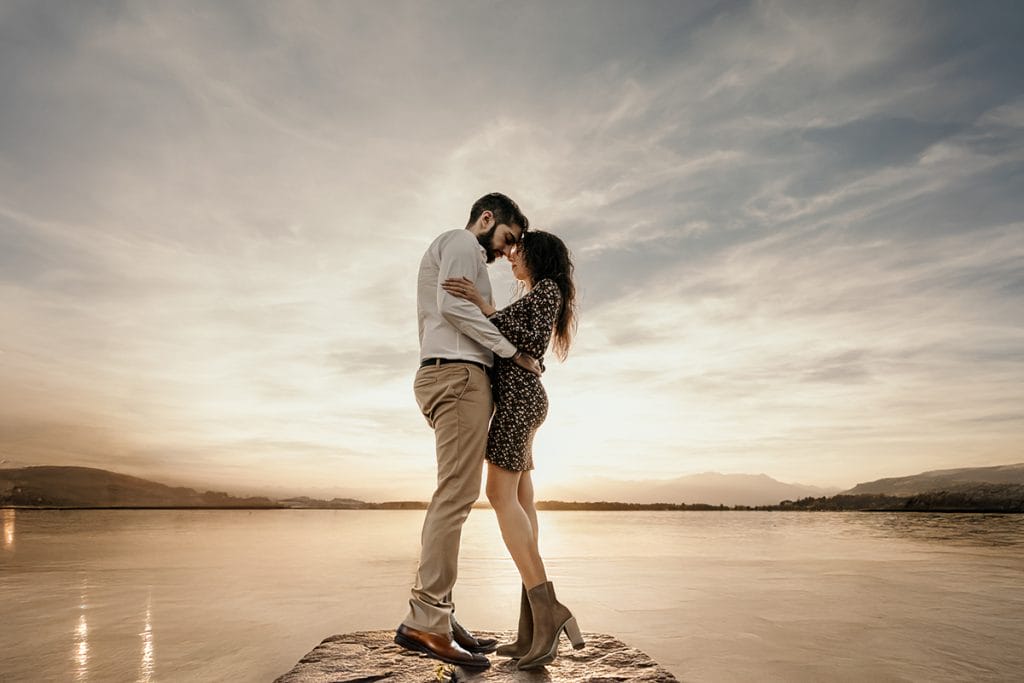 Ilaria and Luca, lost in each other's gaze, stand on a stone pier at Lake Viverone. The setting sun casts a warm glow on the couple, creating a magical moment captured in this pre-wedding photo. 
