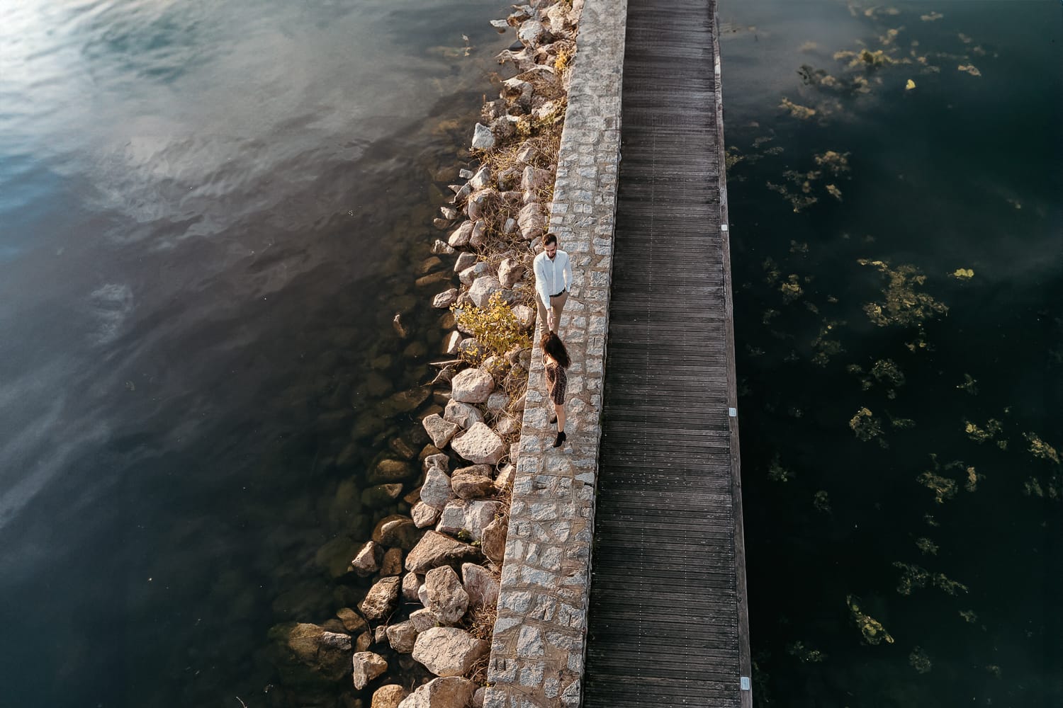 Pre-wedding al Lago di Viverone di Ilaria e Luca. Foto dal drone della coppia che cammina sul pontile di pietra sul lago.