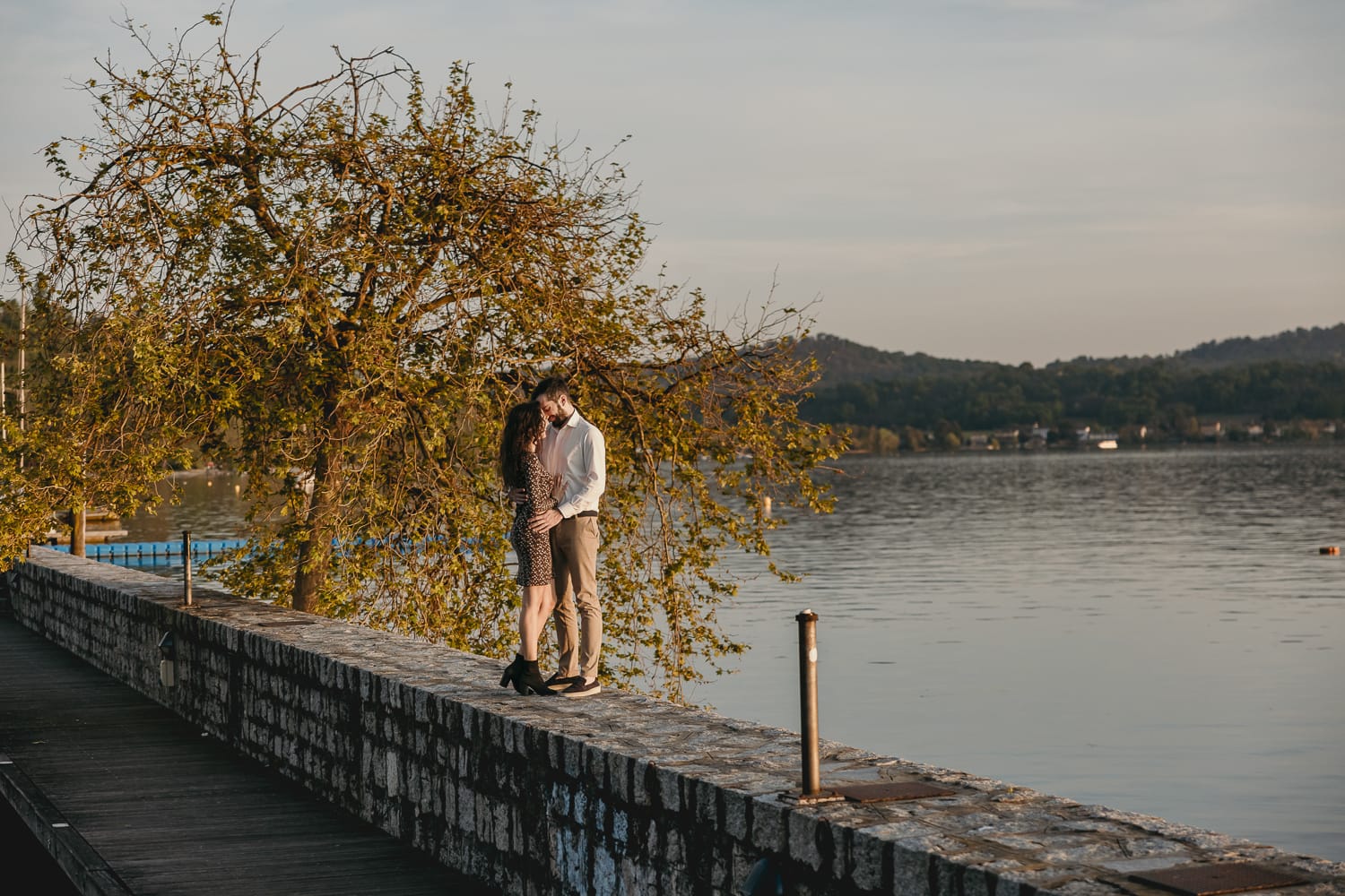 Pre-wedding al Lago di Viverone di Ilaria e Luca. Coppia abbracciata sul pontile di pietra sul lago.