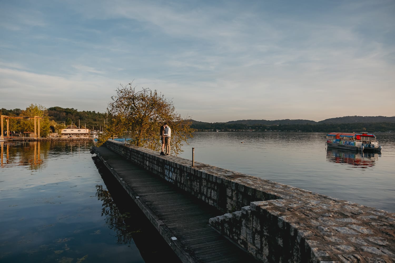Pre-wedding al Lago di Viverone di Ilaria e Luca. Coppia davanti ad un salice sul pontile di pietra sul lago.