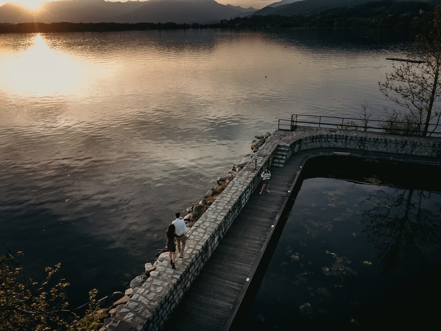 Pre-wedding al Lago di Viverone di Ilaria e Luca. Foto aerea dal drone della coppia che cammina sul pontile di pietra sul lago.
