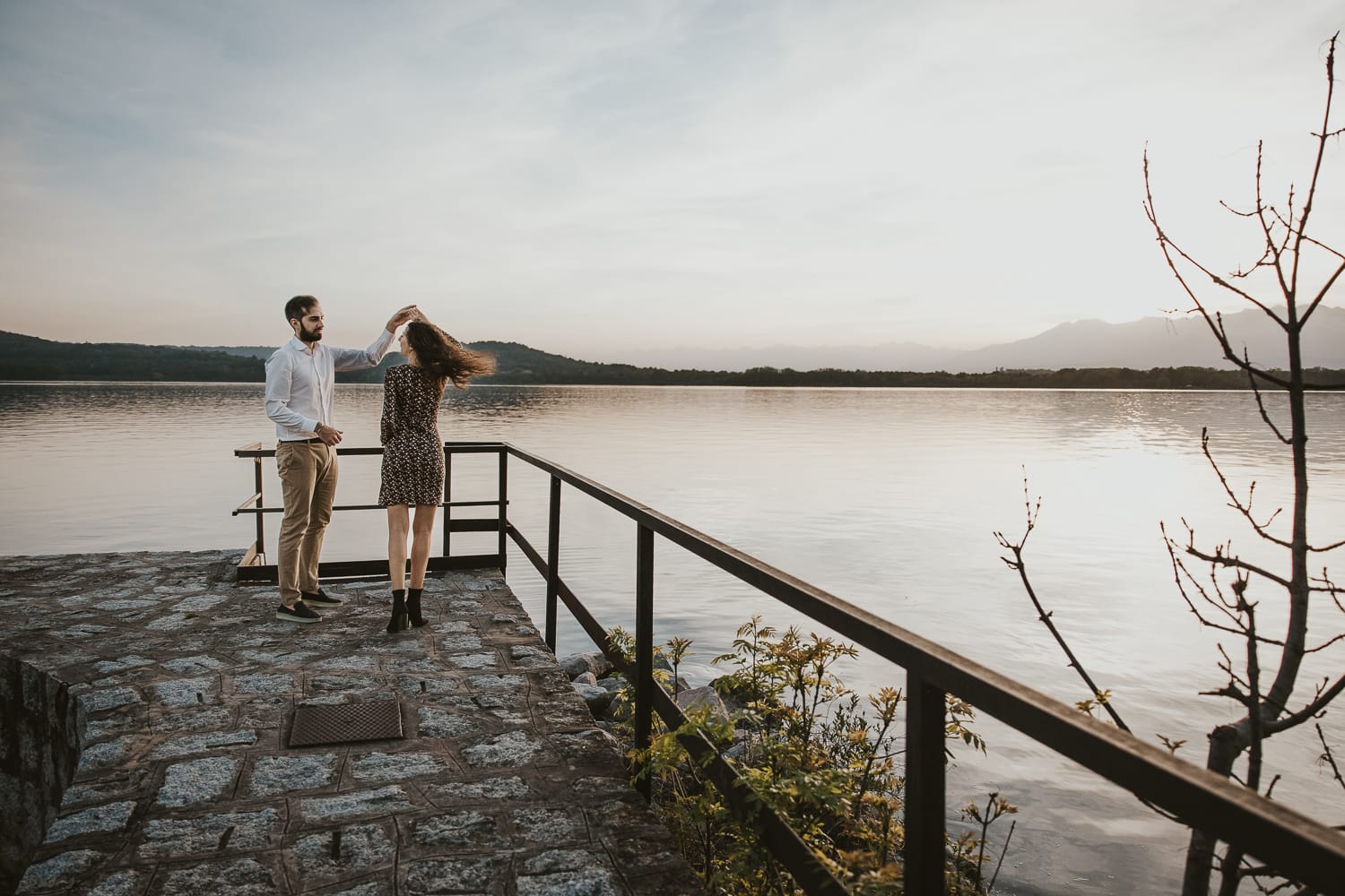Pre-wedding al Lago di Viverone di Ilaria e Luca. Luca fa fare una piroetta a Ilaria sul pontile di pietra.