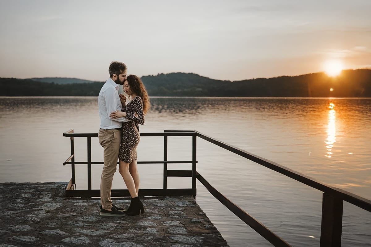 Pre-wedding al Lago di Viverone di Ilaria e Luca. Ilaria e Luca uno di fronte all'altra con sulla sfondo il lago e il sole che tramonta.